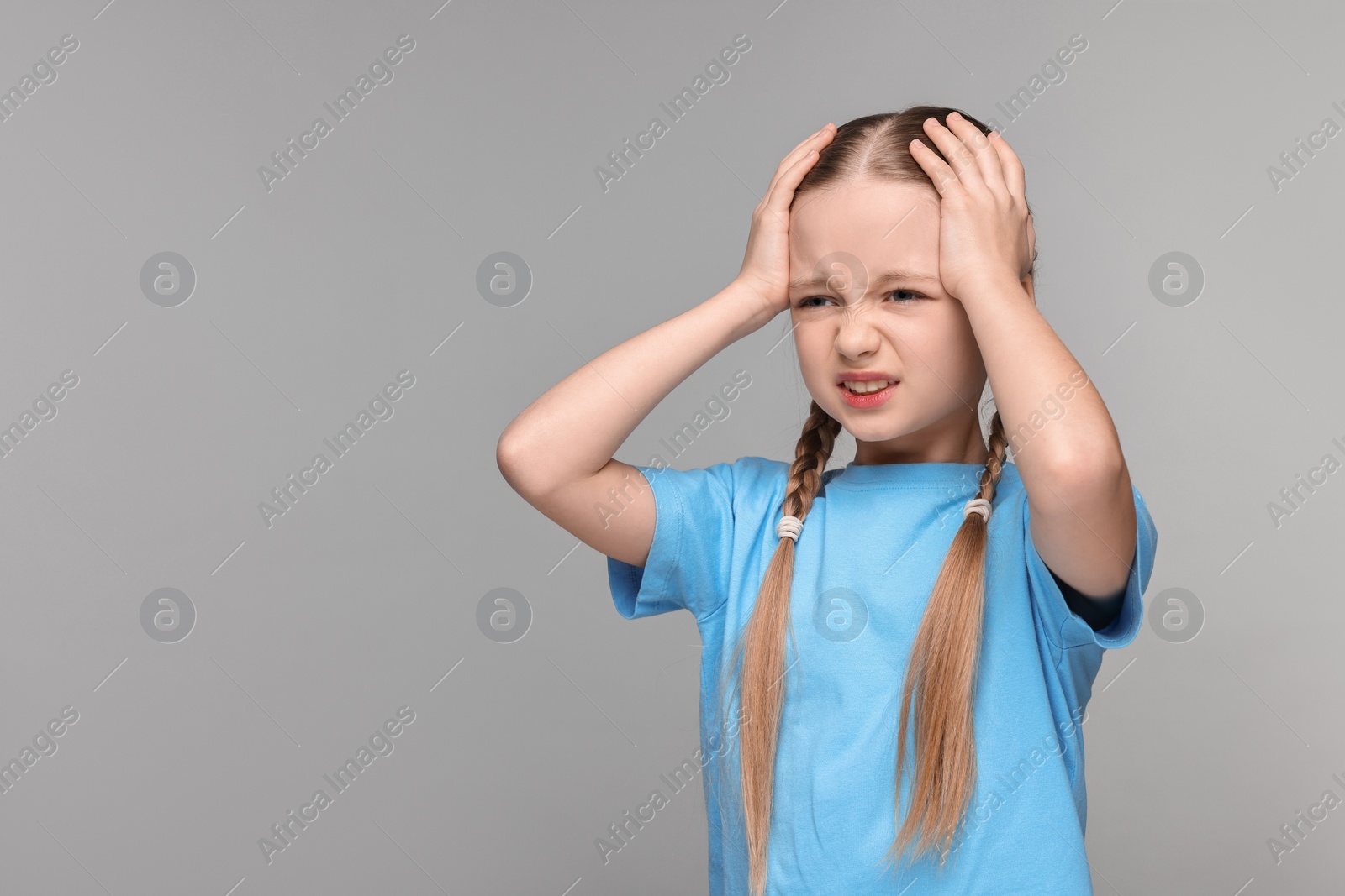 Photo of Little girl suffering from headache on grey background. Space for text