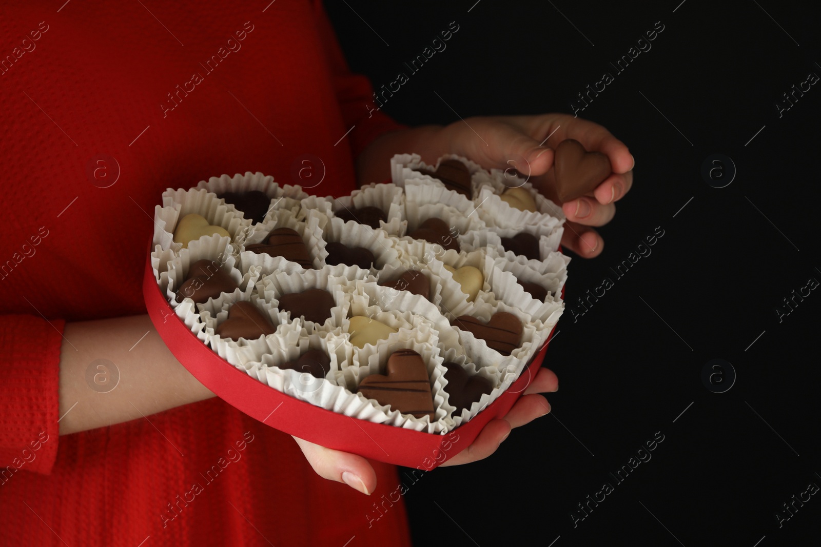 Photo of Woman with box of heart shaped chocolate candies on black background, closeup