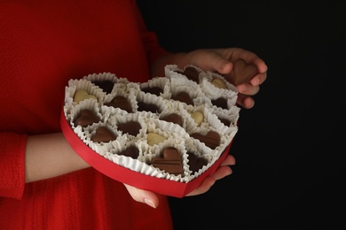 Woman with box of heart shaped chocolate candies on black background, closeup