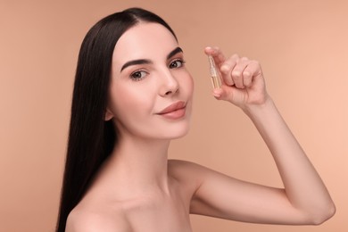 Beautiful young woman holding skincare ampoule on beige background