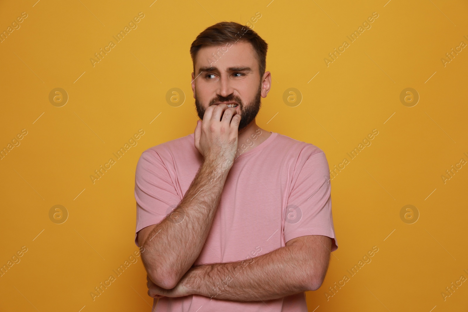 Photo of Man biting his nails on yellow background. Bad habit