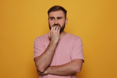 Photo of Man biting his nails on yellow background. Bad habit