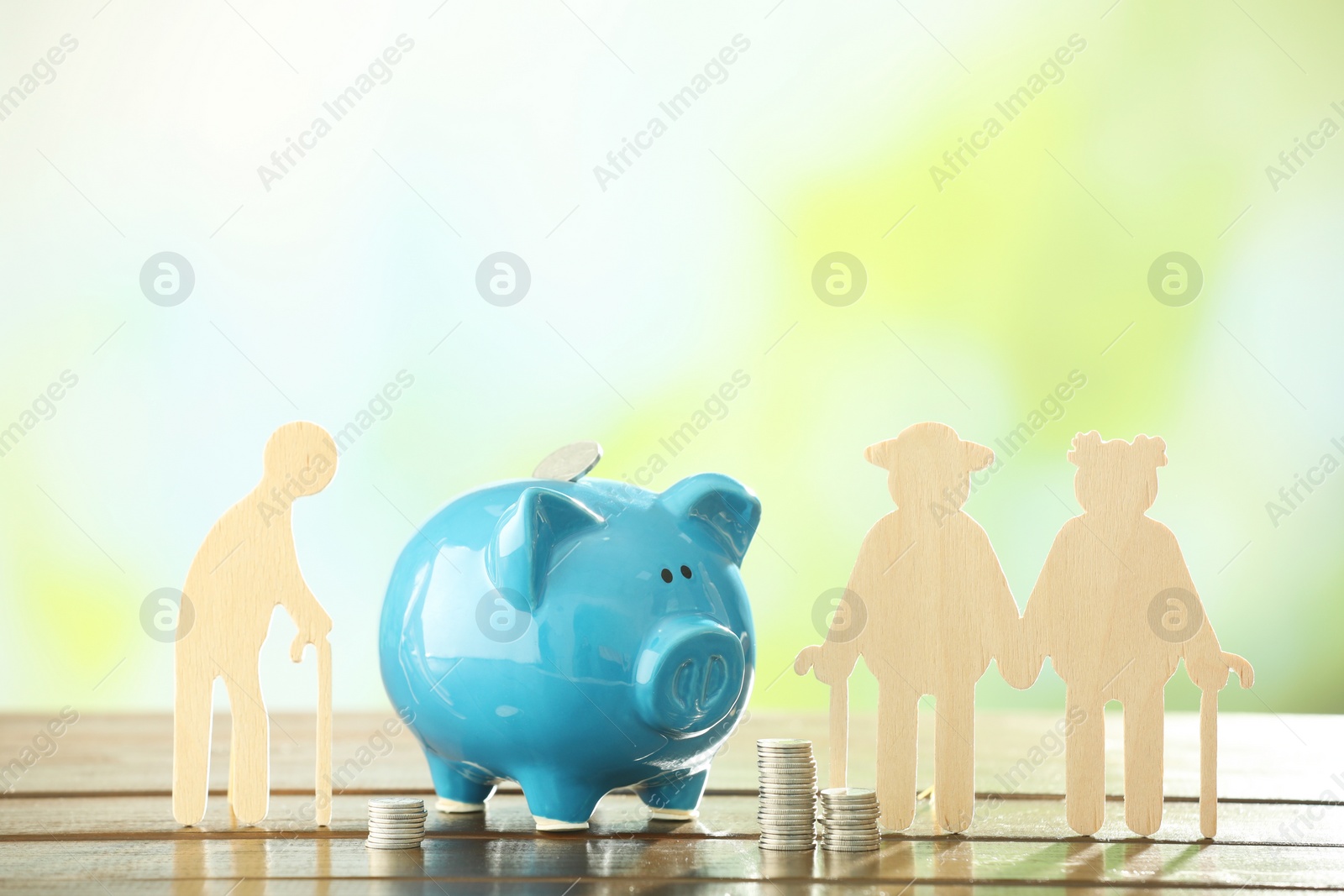 Photo of Pension savings. Figures of elderly people, piggy bank and stacked coins on wooden table against blurred background