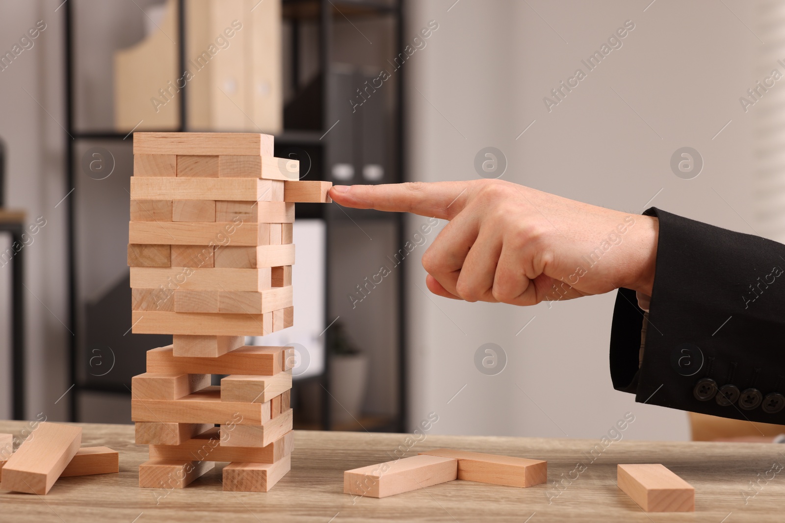 Photo of Playing Jenga. Man building tower with wooden blocks at table indoors, closeup