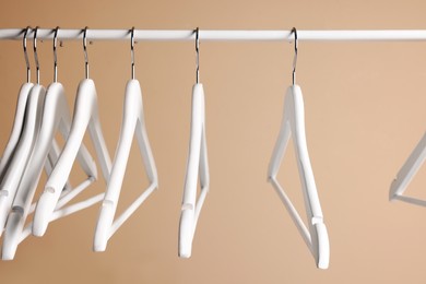 Photo of White clothes hangers on metal rail against beige background