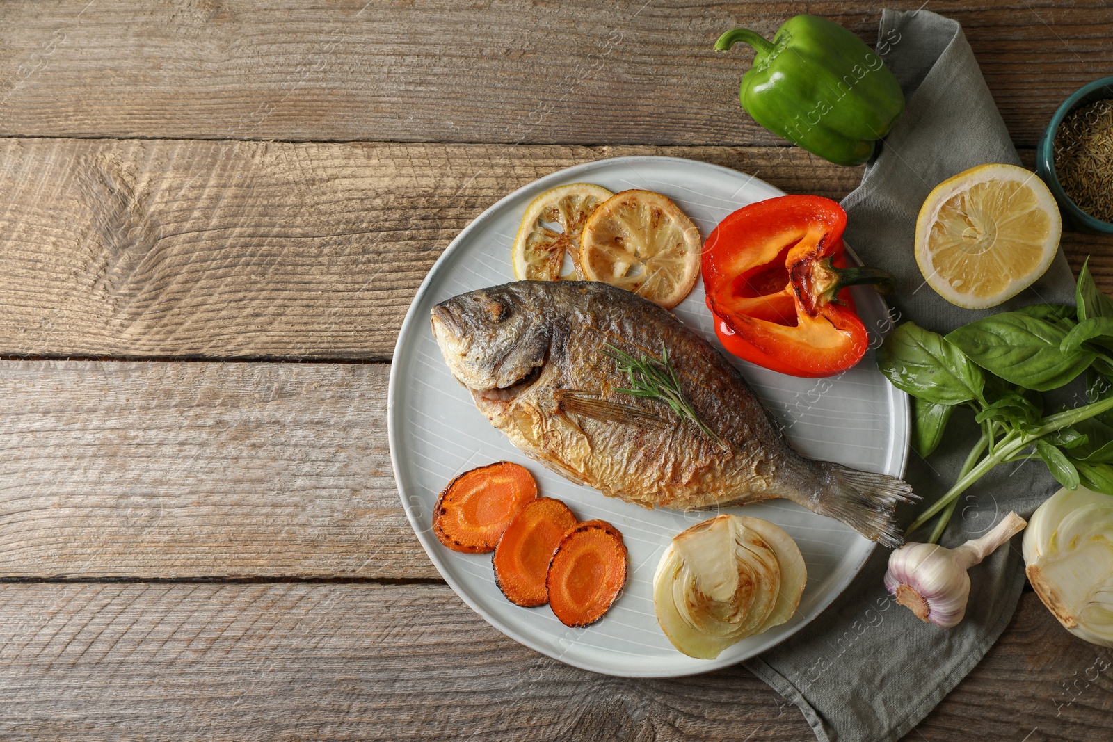 Photo of Delicious dorado fish with vegetables and herbs served on wooden table, flat lay. Space for text