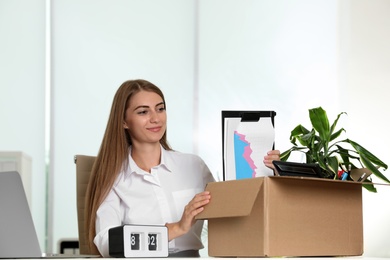 Photo of Happy young woman packing stuff in box at office