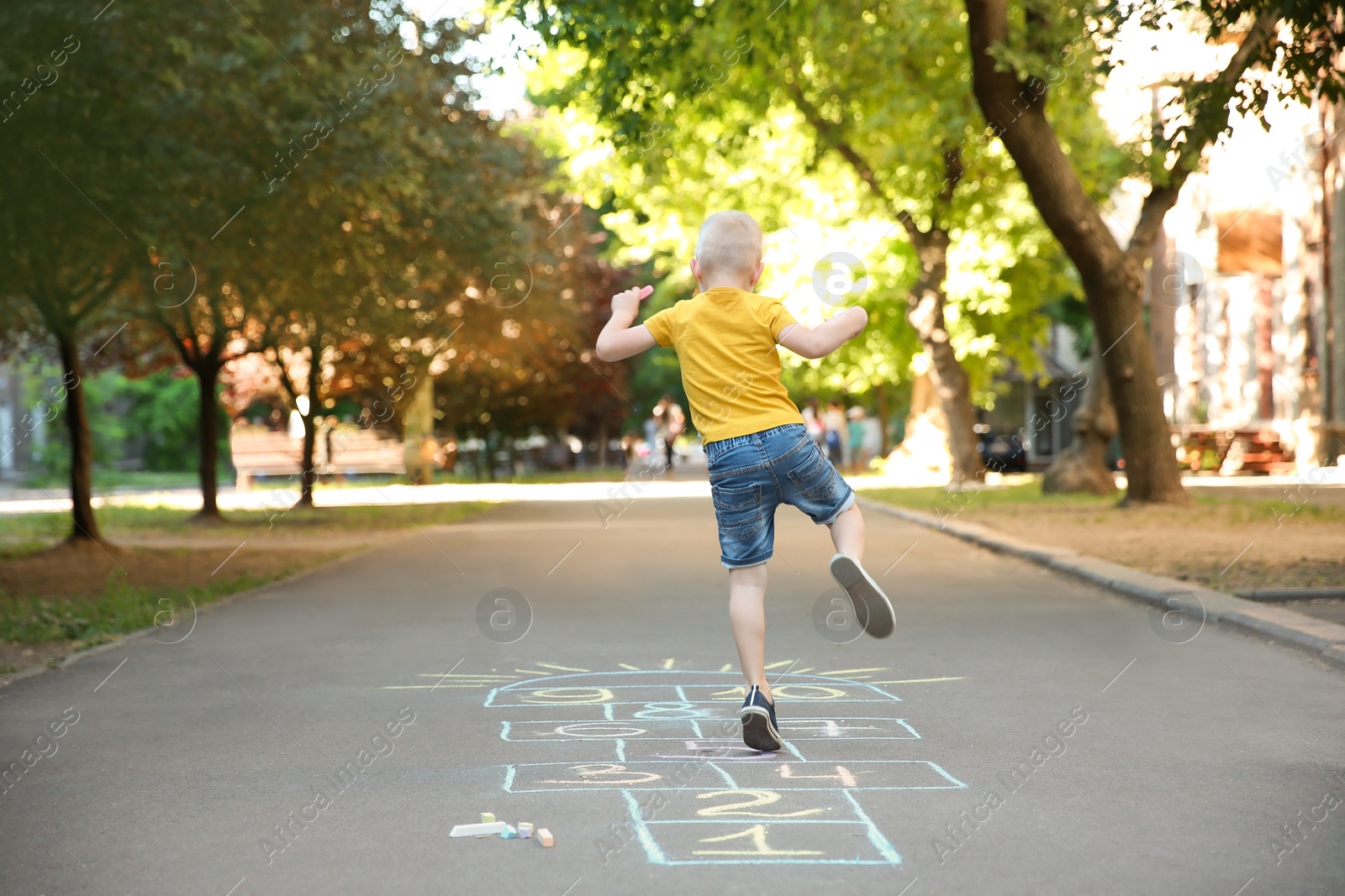 Photo of Little child playing hopscotch drawn with colorful chalk on asphalt