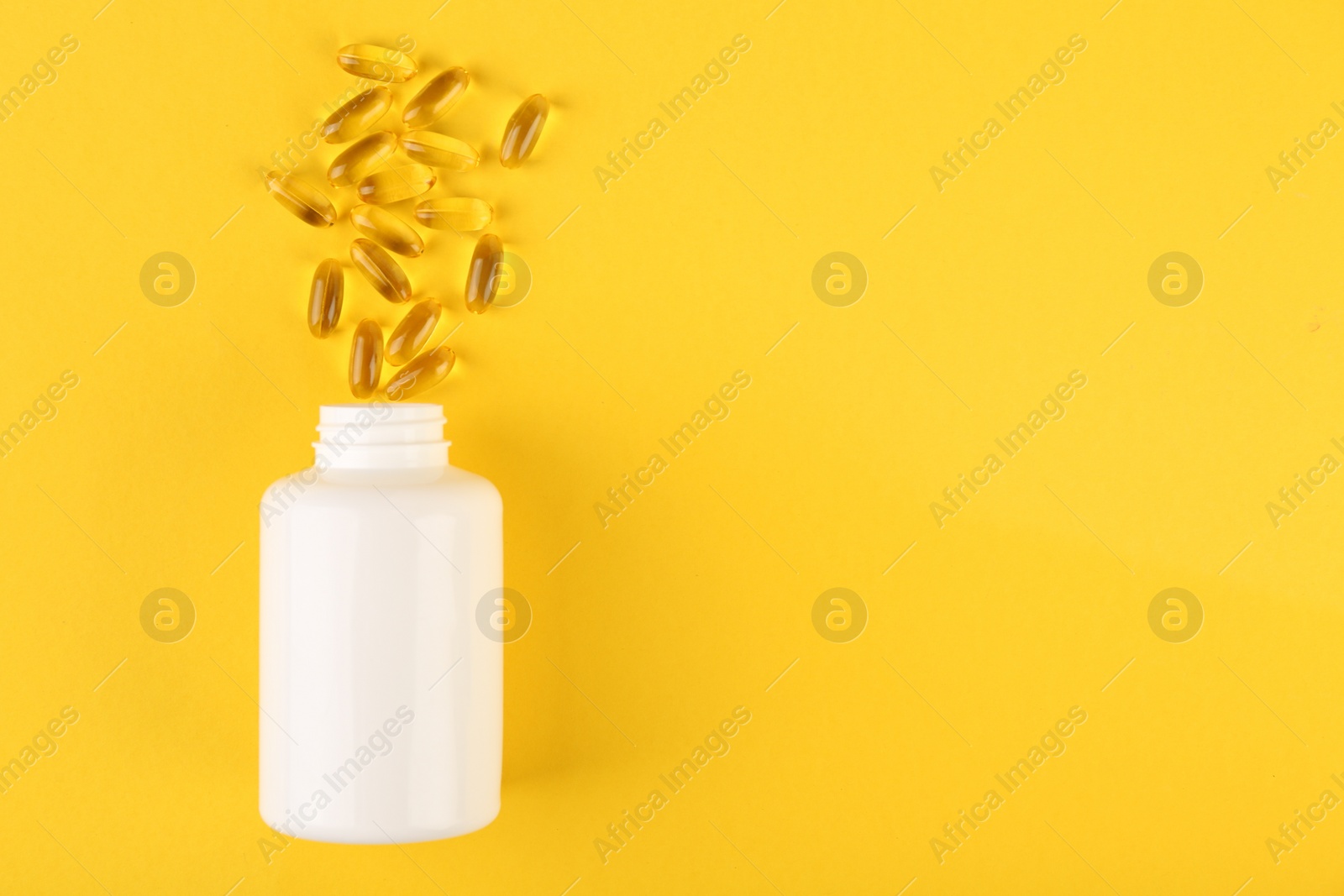 Photo of White medical bottle and vitamin capsules on yellow background, top view. Space for text