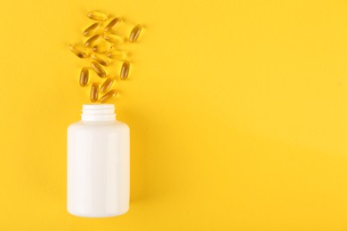 White medical bottle and vitamin capsules on yellow background, top view. Space for text