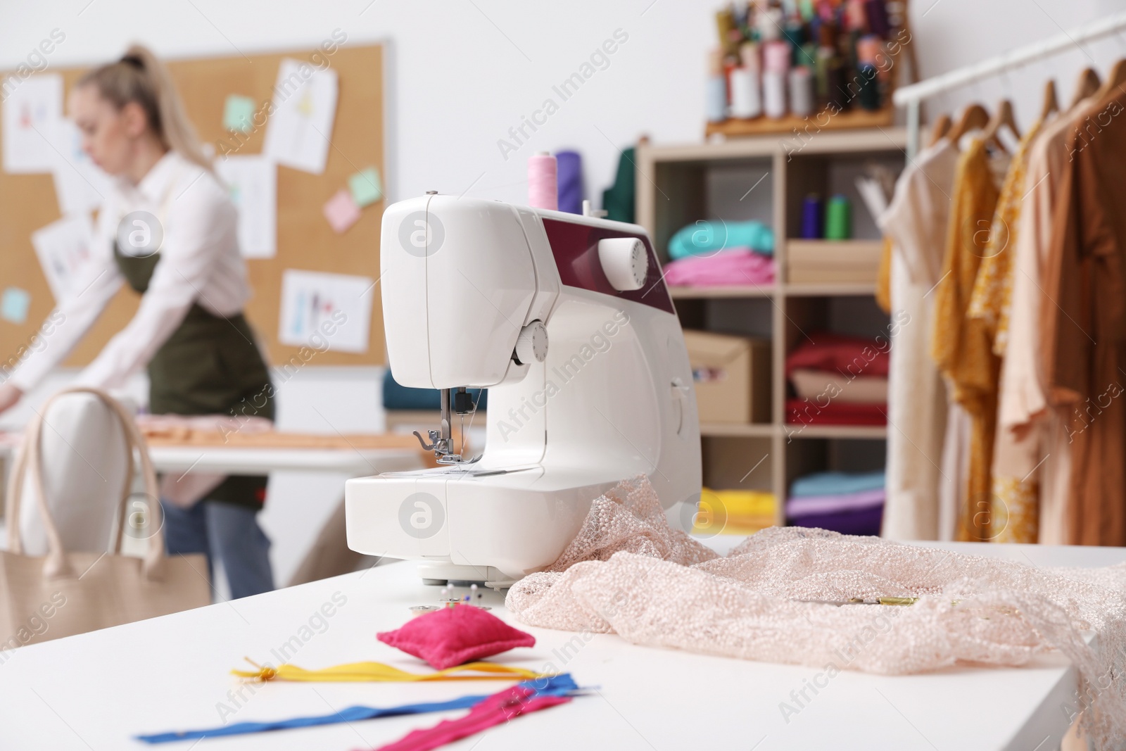 Photo of Dressmaker working in atelier, focus on table with sewing machine and accessories