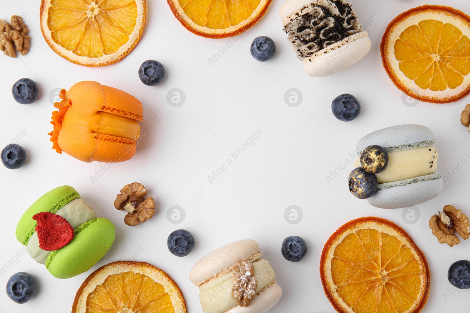 Photo of Frame made of delicious macarons, dry orange slices and blueberries on white table, flat lay. Space for text