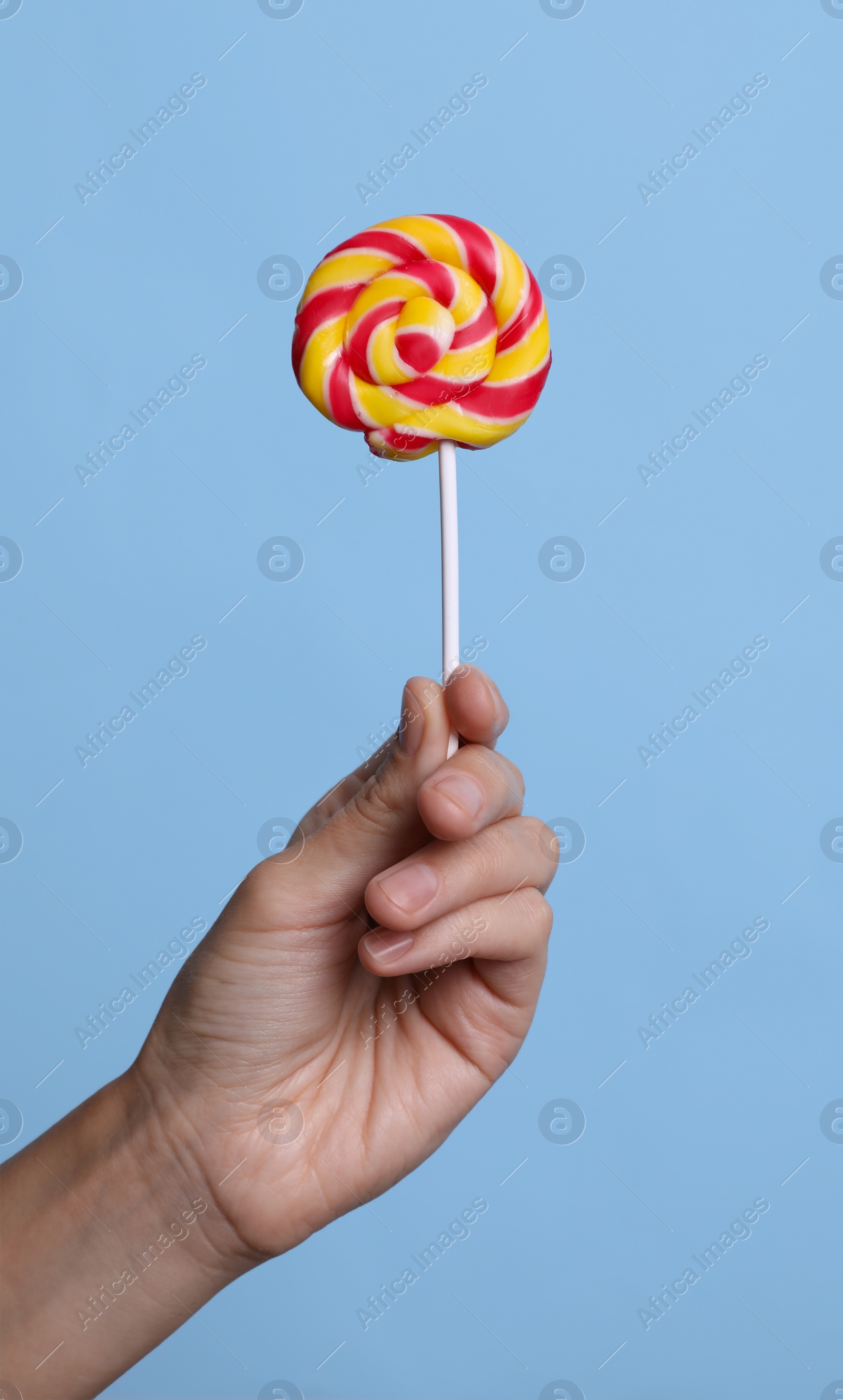 Photo of Woman holding bright tasty lollipop on light blue background, closeup