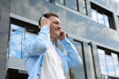 Photo of Smiling man wearing headphones near building outdoors
