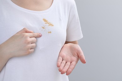 Woman showing stain on her t-shirt against light grey background, closeup