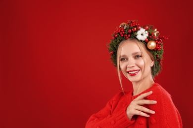 Beautiful young woman wearing Christmas wreath on red background. Space for text