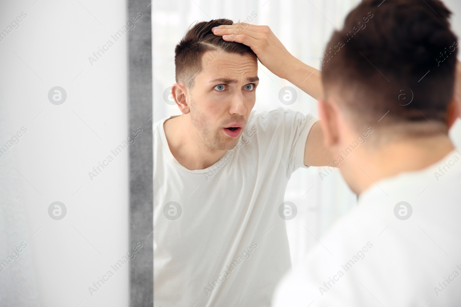 Photo of Young man with hair loss problem looking in mirror indoors