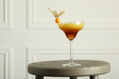 Photo of Refreshing cocktail decorated with physalis fruit on wooden table indoors. Space for text