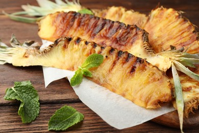 Tasty grilled pineapple pieces and mint leaves on wooden table, closeup