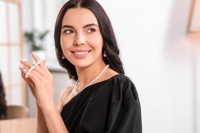 Young woman wearing elegant pearl jewelry indoors, space for text