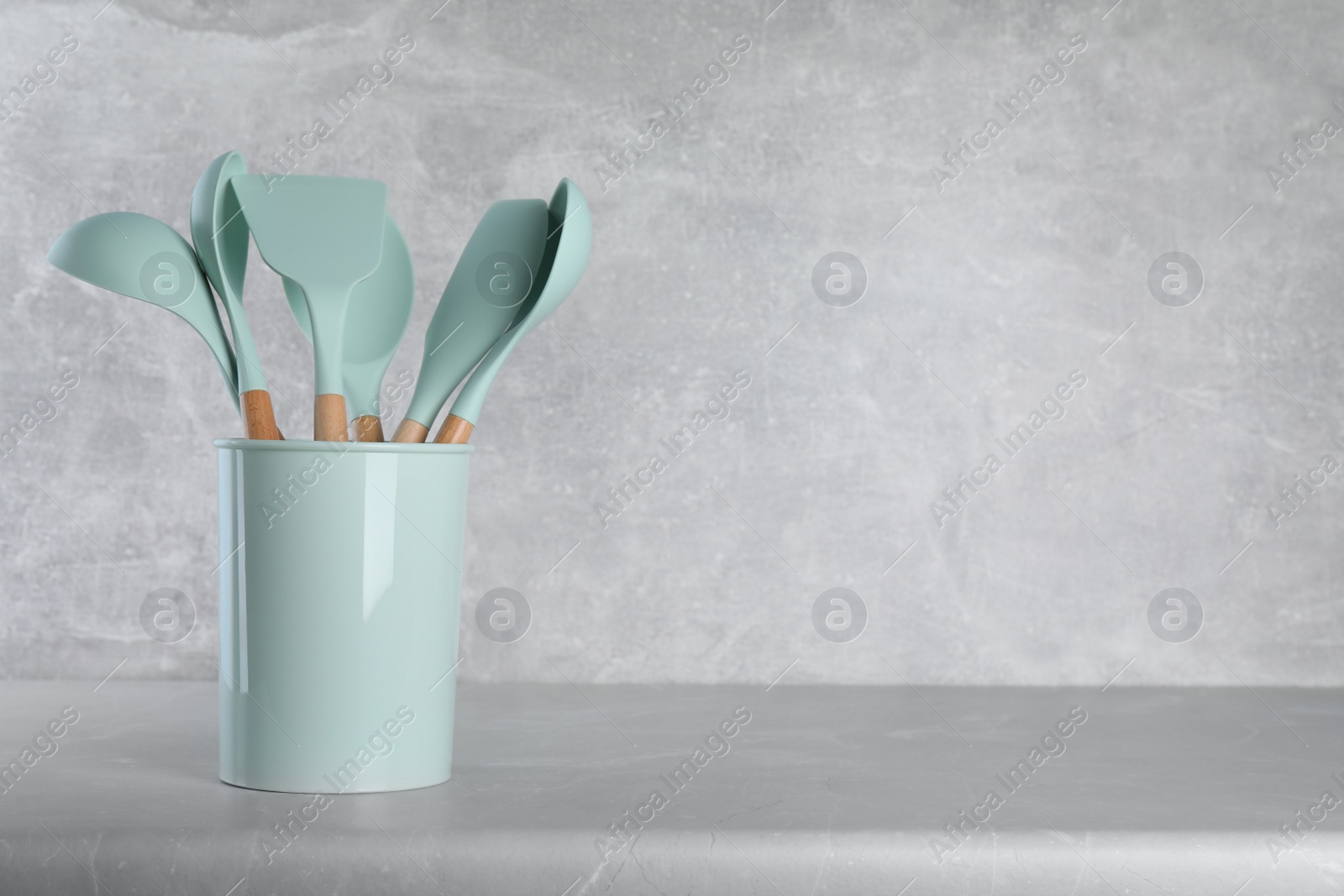 Photo of Holder with kitchen utensils on grey table. Space for text