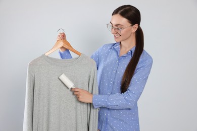 Photo of Woman cleaning clothes with lint roller on light grey background