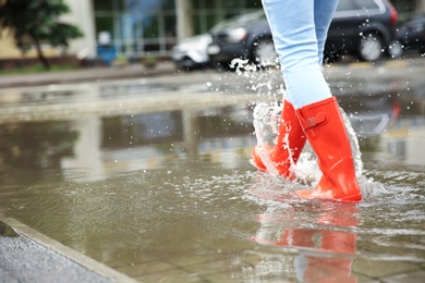 Photo of Woman with red rubber boots in puddle, closeup. Rainy weather