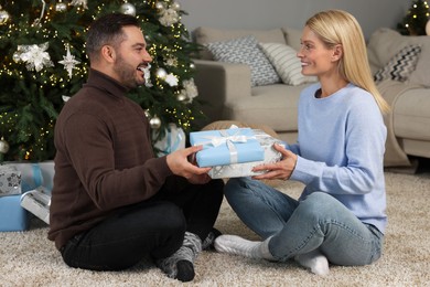 Happy couple exchanging Christmas gifts at home