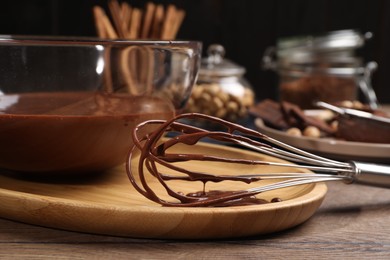 Bowl and whisk with chocolate cream on wooden table, closeup