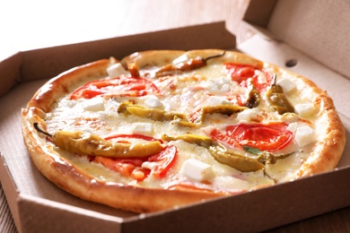 Cardboard box with tasty pizza on table, closeup