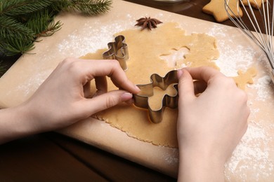 Photo of Woman making Christmas cookies with cutters at wooden table, closeup