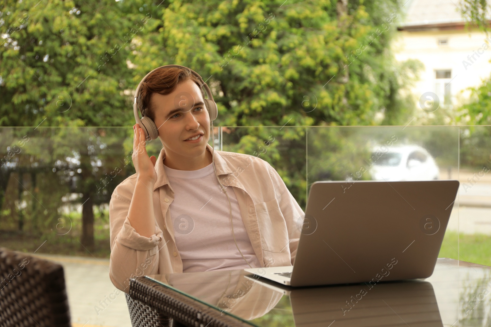 Photo of Handsome young man with headphones working on laptop in outdoor cafe