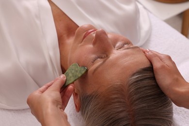 Photo of Woman receiving facial massage with jade gua sha tool in beauty salon, closeup