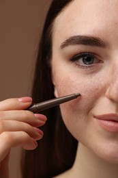 Photo of Beautiful woman drawing freckles with pen on brown background, closeup