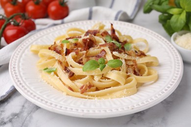 Photo of Tasty pasta with bacon and basil on white marble table, closeup