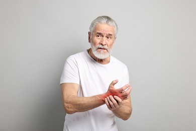 Image of Senior man suffering from pain in wrist on grey background