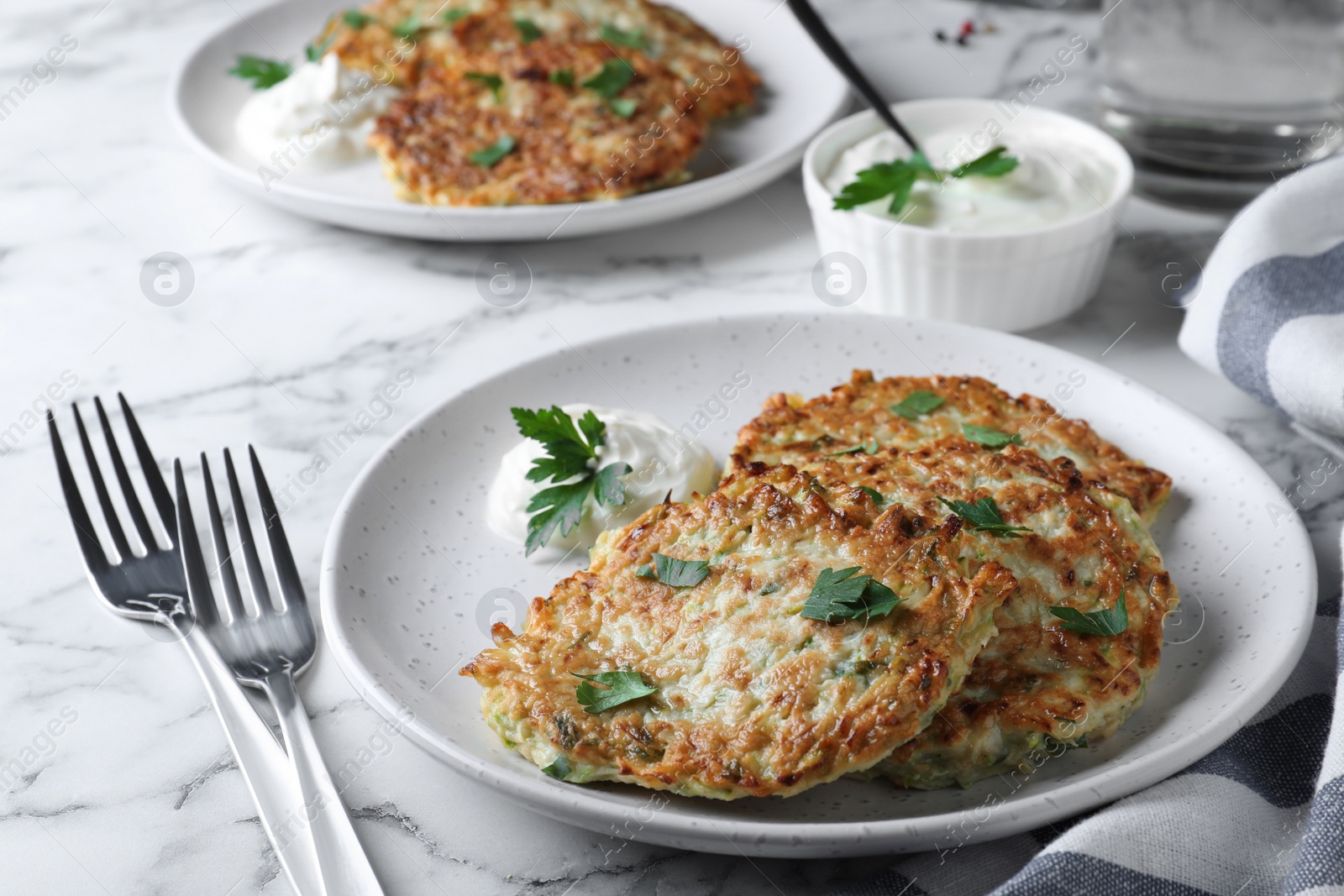 Photo of Delicious zucchini fritters served on white marble table, closeup