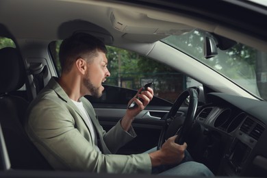 Photo of Stressed businessman talking on phone in driver's seat of modern car