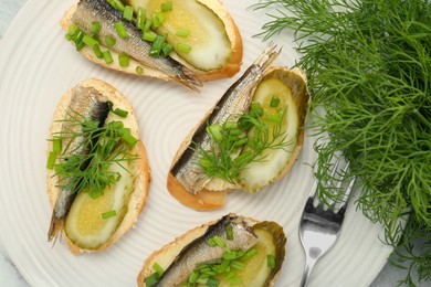 Photo of Delicious sandwiches with sprats, pickled cucumber, green onion and dill on plate, top view