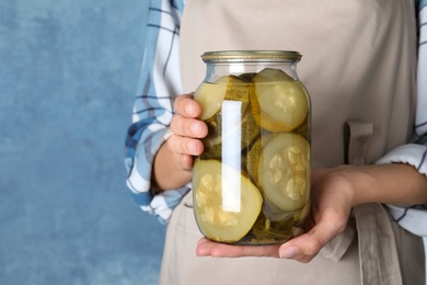 Photo of Woman holding jar with pickled zucchinis against blue background, closeup