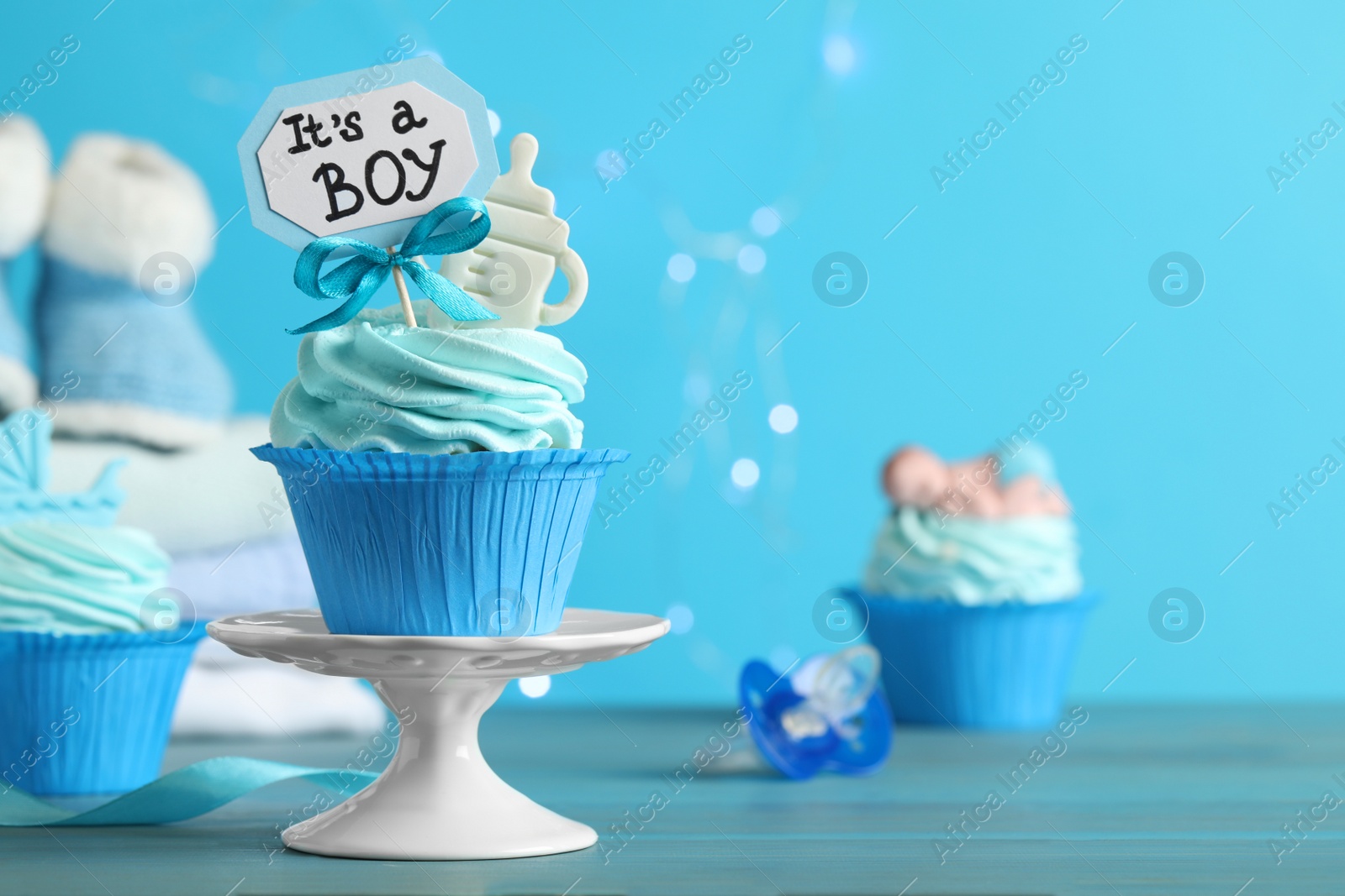 Photo of Beautifully decorated baby shower cupcake with cream and boy topper on light blue wooden table. Space for text