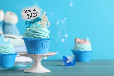 Beautifully decorated baby shower cupcake with cream and boy topper on light blue wooden table. Space for text