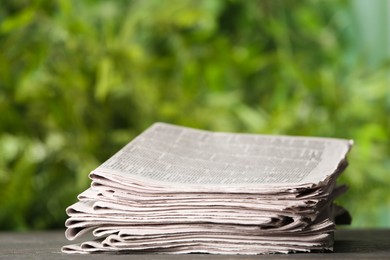 Photo of Stack of newspapers on grey table against blurred green background. Journalist's work