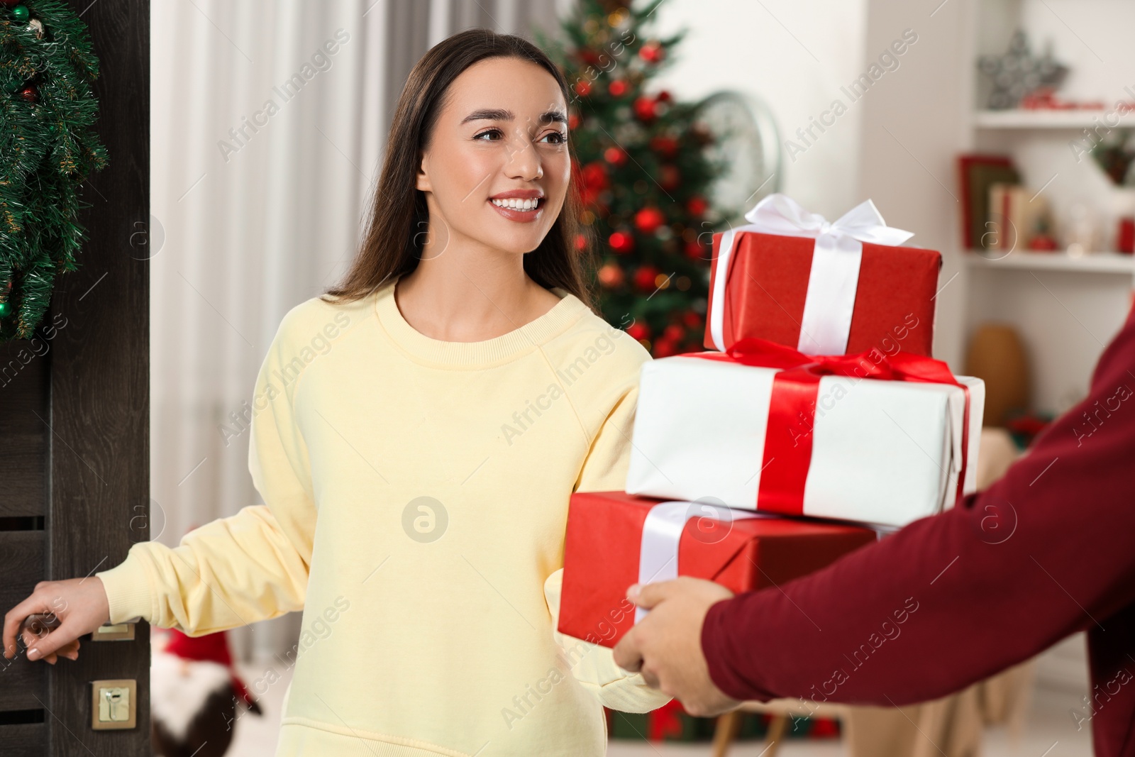 Photo of Courier giving young woman Christmas gift boxes indoors. Sending present by mail