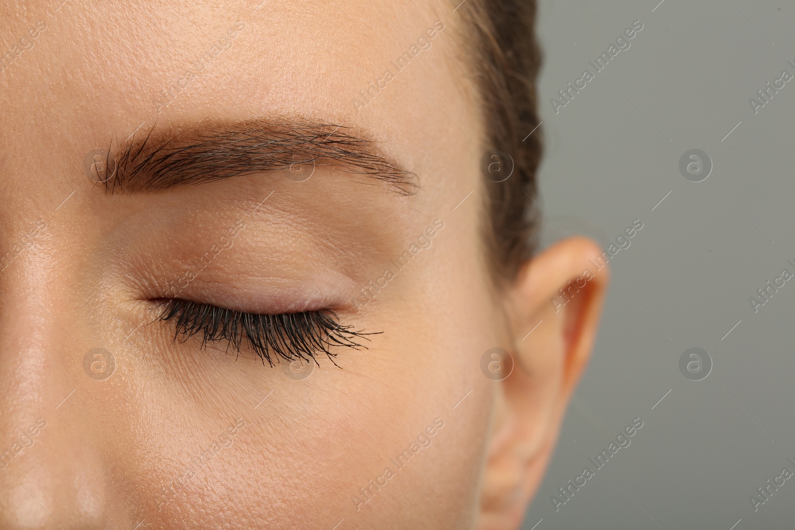 Photo of Woman with long eyelashes after mascara applying against grey background, closeup