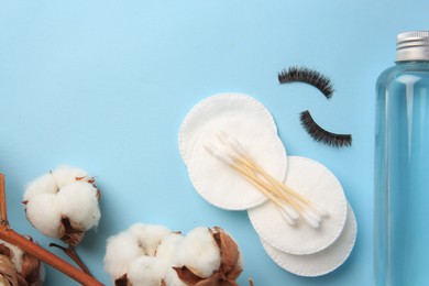 Photo of Bottle of makeup remover, cotton flowers, pads, swabs and false eyelashes on light blue background, flat lay. Space for text