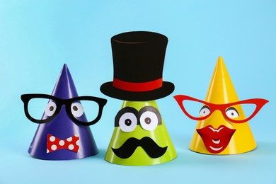 Photo of Handmade party hats with funny faces on light blue background