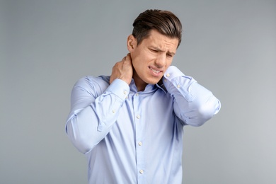 Young man suffering from neck pain on grey background