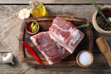 Photo of Pieces of raw pork belly, oil, garlic, salt and spices on wooden table, flat lay