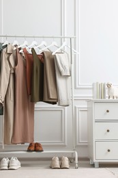 Photo of Rack with different stylish women`s clothes, shoes and dresser near white wall in room